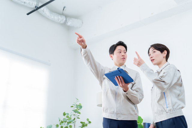 作業服姿のスタッフ2名が室内の天井設備をタブレットで確認している様子