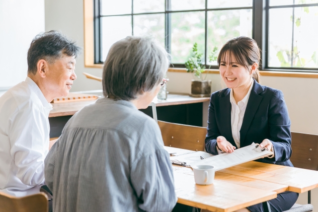 女性スタッフが笑顔で高齢のご夫婦に資料を見せながら相談対応する様子